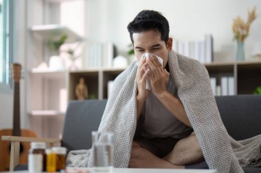 Genç bir adam battaniyenin altında oturup burnunu siliyor. Soğuk algınlığı ya da grip belirtileri gösteriyor. Sağlığa ve sağlığa odaklan..