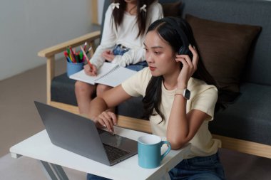 Odaklanmış genç bir kadın evinde rahat bir şekilde otururken bilgisayarını ve kulaklıklarını kullanarak uzaktan öğrenme ile meşgul oluyor..
