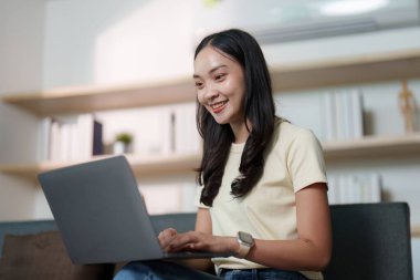 Genç bir kadın evde dizüstü bilgisayarla çalışmaktan zevk alıyor. Olumlu bir uzaktan çalışma deneyimi yansıtıyor..