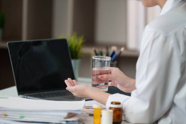 Genç bir kadın, yoğun bir çalışma ortamında su ve sağlığın önemini vurgulayarak bir bardak su tutuyor..