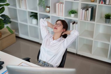 Genç bir kadın sandalyesine yaslanıyor, gözleri kapalı, masasında huzur dolu bir anın tadını çıkarıyor..