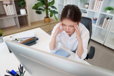 Genç bir kadın masasında baş ağrısıyla boğuşuyor, ofis işinin ve akıl sağlığının zorluklarını vurguluyor..