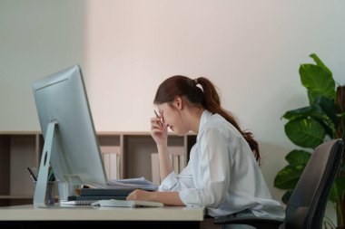 Genç bir kadın masasında çalışırken bunalma belirtileri gösteriyor. İşyeri stresinin akıl sağlığı üzerindeki etkisini vurguluyor..