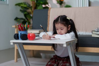 Masada ödevlerini yapmaya odaklanmış, etrafı defterler ve elmalarla çevrili, verimli bir çalışma ortamını ön plana çıkaran bir kız..