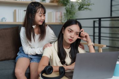 Genç bir kız, dizüstü bilgisayarda çalışırken ablasını rahatlatıyor. Ev ortamında kardeş desteğini vurguluyor..