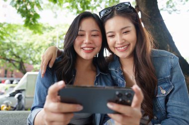 İki arkadaş kahvenin keyfini çıkarırken gülüyorlar ve sohbet ediyorlar. Açık havada güçlü dostluklarını vurguluyorlar..