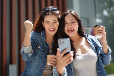 İki arkadaş neşeli bir anı paylaşıyor, gülümseyen ve tezahürat yapan, akıllı bir telefona bakan, arkadaşlığı ve mutluluğu somutlaştıran.