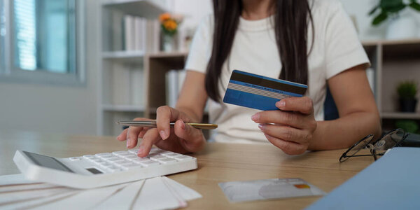 A young woman holds a credit card while using a calculator to manage her finances, showcasing modern budgeting techniques.