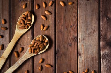 Badem bir cam kase ve taneli ahşap zemin üzerine tahta kaşıklar. Üstten görünüm.