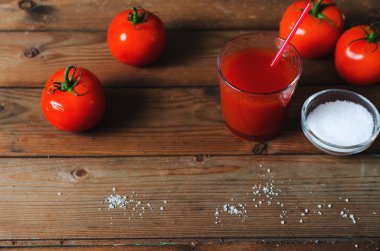 Taze domates ve tuz ile bardak domates suyu. Rustik ahşap arka plan.