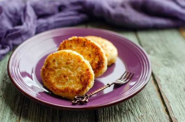 Cottage cheese pancakes on a dark background. Syrniki with fresh mint. Pancakes with cottage cheese on a lilac plate. Homemade food