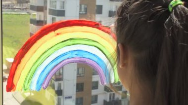 Evdeki karantina sırasında pencereye gökkuşağı çizen kız.