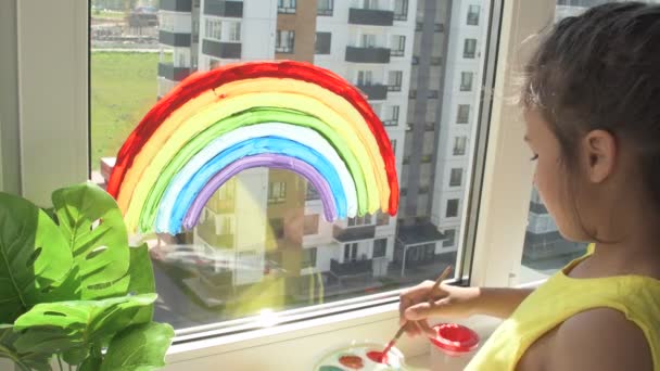 Chica pintando arco iris en la ventana durante la cuarentena en casa. — Vídeo de stock