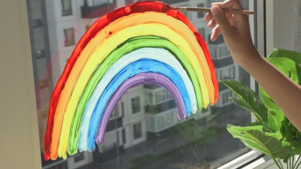 Девушка рисует радугу на окне во время карантина дома. — стоковое видео