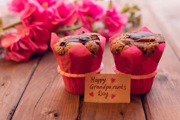 Bonita tarjeta con flores de malva roja y dos magdalenas y caja y etiqueta artesanal. — Foto de Stock