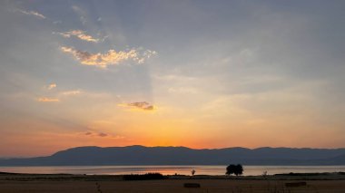 Kuru bir tarlanın önündeki dağların ve gölün üzerinde muhteşem bir günbatımı manzarası..