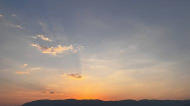 Huzurlu bir günbatımı manzarası: Dağların ve suyun üzerindeki ılık renkli gökyüzü.