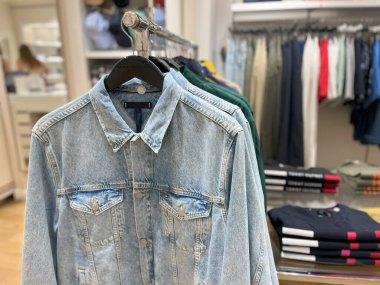 Askılarda kot ceketler ve diğer kıyafetlerin sergilendiği bir giyim mağazasının fotoğrafı..