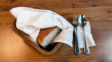 Yemek masasında bir sepet taze ekmek. Restoranda, çatal ve tabağın yanında, havluya sarılmış bir sepet taze ekmek..