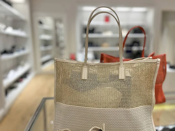 Mağaza ortamında bej dokunmuş bir el çantasını gösteren bir fotoğraf..