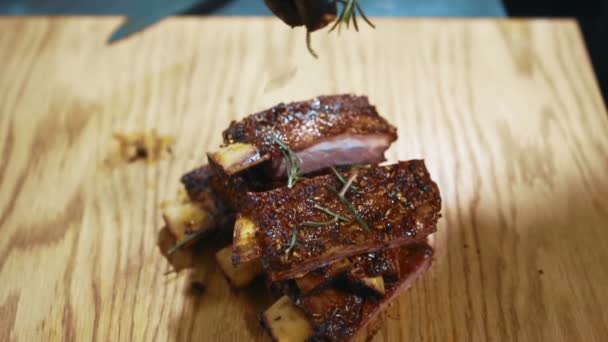 Na dřevěný stůl ruční sypání rozmarýnu na horké maso s kostí. — Stock video