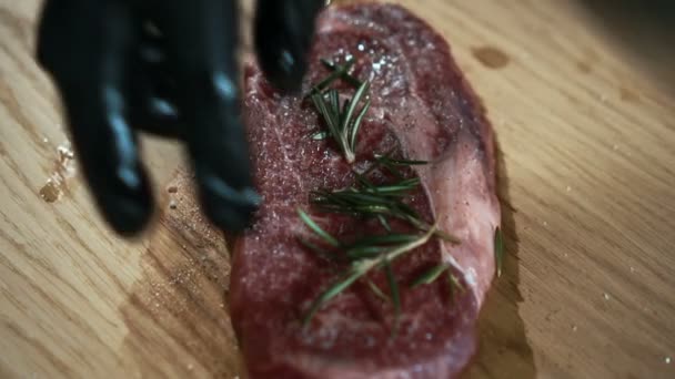 Γκρο πλαν του μάγειρα ψεκάζει ένα κομμάτι από το ωμό κρέας με βότανα. — Αρχείο Βίντεο