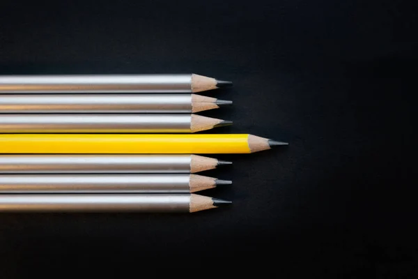 one lead pencil different from others on a black background