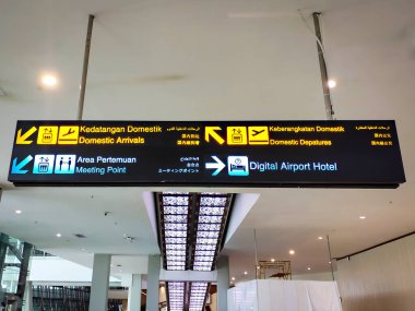 Jakarta, Endonezya - 11 Mayıs 2025: Cakarta, Endonezya 'daki Soekarno Hatta Uluslararası Havalimanı' nda yer alan çok dilli çevirilerle aydınlık, neon havalimanı bilgi levhasının düşük açılı bir görüntüsü.