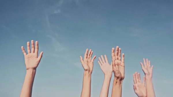 People rasing hands on blue sky background. Voting, democracy or volunteering concept