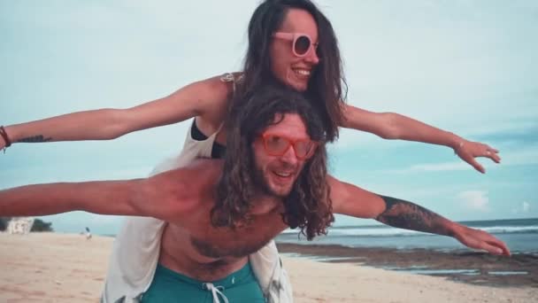 Närbild porträtt av en attraktiv ung och energisk par ha kul på stranden. Kvinna piggyback rider en man och skrattar. Resor och semester koncept. — Stockvideo