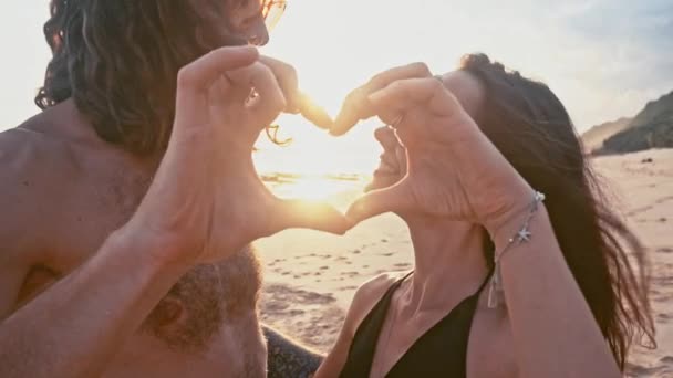 Atraente, apaixonado, belo jovem casal de viagem desfrutando do pôr do sol na praia beijando de mãos dadas e fazendo uma forma de coração em câmera lenta. Sea Summer Vacation Concepção de turistas românticos felizes . — Vídeo de Stock