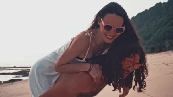 Close up portrait of a attractive young and energetic couple having fun on the beach. Woman piggyback riding a man and laughing. Sea Summer Vacation Happy Romantic Tourists concept — Stock Video