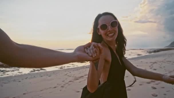 Jovem casal de mãos dadas mulher levando namorados caminhando em direção ao pôr do sol na praia vazia POV conceito de viagem — Vídeo de Stock