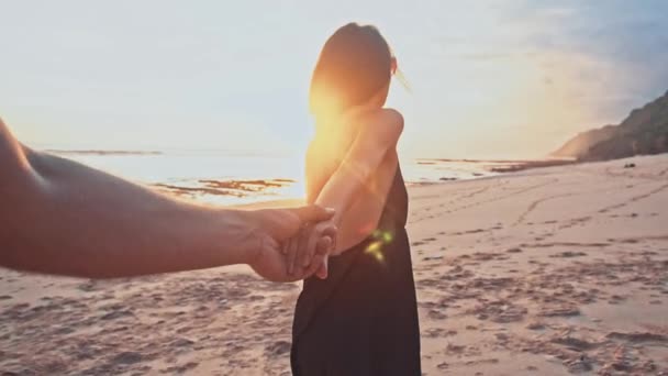 Trzymając się za ręce kobieta spaceru w kierunku zachód słońca na pustej plaży wiodących chłopaków młoda para. Morze lato wakacje podróż romantyczny szczęśliwy koncepcja — Wideo stockowe