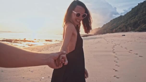 Молода пара тримає руку жінці, що веде хлопців, що йдуть до заходу сонця на порожньому пляжі. Морські літні канікули щаслива концепція романтичних подорожей — стокове відео