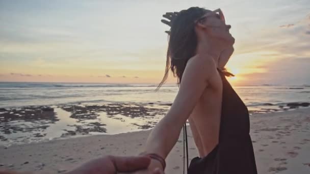 Молодая пара держит за руки женщину, ведущую парней, идущих к закату на пустой пляж. Морские каникулы счастливой романтической концепции путешествия — стоковое видео