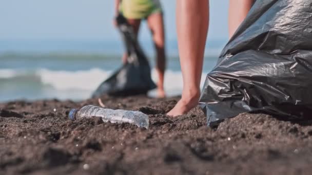 Grupo de voluntarios limpiando la playa. El voluntario levanta y lanza una botella de plástico en la bolsa. Concepto de voluntariado y reciclaje. Espacio de copia del concepto de conciencia ambiental — Vídeo de stock