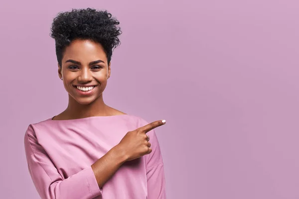 Retrato horizontal de feliz escuro pele mista modelo feminino indica com dedo indicador no espaço de cópia em branco, mostra lugar para o seu anúncio ou texto promocional. Linda menina afro-americana — Fotografia de Stock