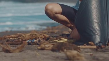 Closeup gönüllü sit ve sahilde çöp toplamak. Siyah plastik torba içine deniz sahilde temiz toplama çöp. Plaj Temizleme gönüllüler. Gönüllü ve kavram geri dönüşüm