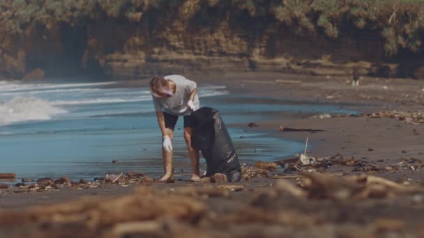 Freiwillige sammeln Müll am schwarzen Sandstrand in schwarzen Plastiktüten ein. Freiwillige säubern den Strand. Müll am Strand aufräumen. Umweltbewusstes Konzept — Stockvideo