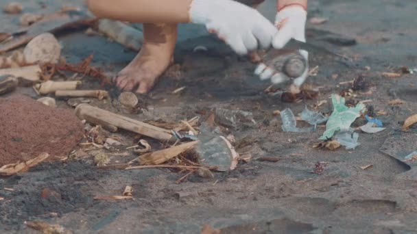 Närbild av frivilliga sitta och plocka upp skräp på stranden. Renare samla skräp på sea beach i svart plastpåse. Frivilliga rengöring stranden. Städa upp skräp på stranden — Stockvideo