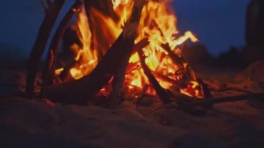 Sahilde kamp ateşi yaz akşamı sırasında yanan. Arka plan olarak doğada şenlik ateşi. Ahşap beyaz kum kıyısında günbatımında yanan. seçici odak. deniz su kenarı yakınındaki tropikal romantik manzara.