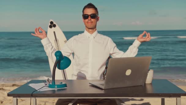 Tranquilo hombre de negocios relajante meditación practicando en el lugar de trabajo en la playa — Vídeo de stock
