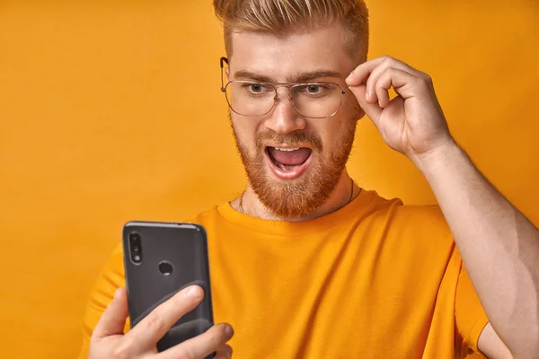 Shocked man with red beard keeps jaw dropped, received message on phone