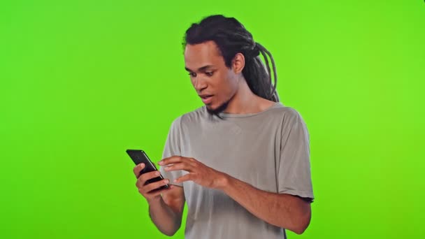 Maschio dalla pelle scura con dreadlocks sembra agitato allo schermo dello smartphone — Video Stock