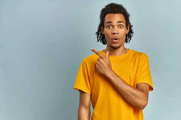 Förvånad afroamerikanska manliga hipster, håller munnen öppen, vara stupefied som annonserar något, bär fashionabla orange t-kort, indikerar med pekfingret i det övre högra hörnet. Omg-konceptet. — Stockfoto