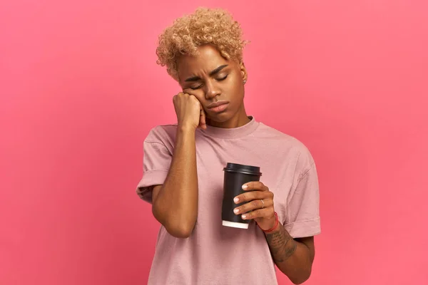 Só o café pode refrescar-me. Cansado sonolento afro-americano mulher cobre metade do rosto com palma, tem expressão triste, fecha os olhos, carrega copo descartável de bebida com cafeína, tem continuar trabalhando . — Fotografia de Stock