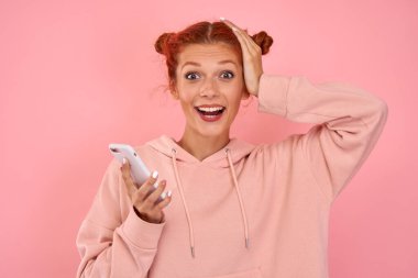 Neşeli, duygusal, azgın, günlük giysiler içinde beyaz bir kız akıllı telefon tutuyor.