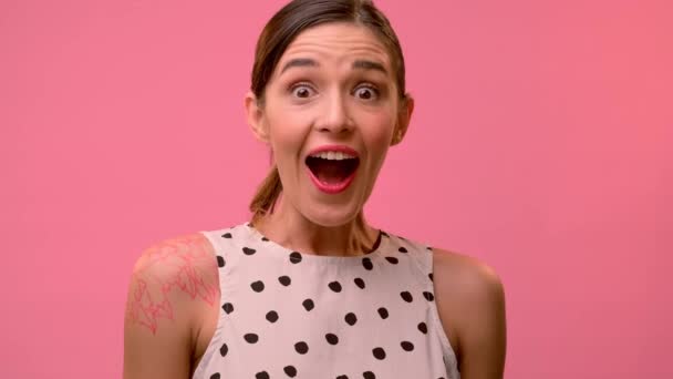 Mujer feliz sorprendida por algo en un fondo de pared rosa. — Vídeos de Stock