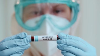 Doktorun elinde parlak arkaplanda kovid 19 antikorları olan test tüpünü tutarken yakın plan..